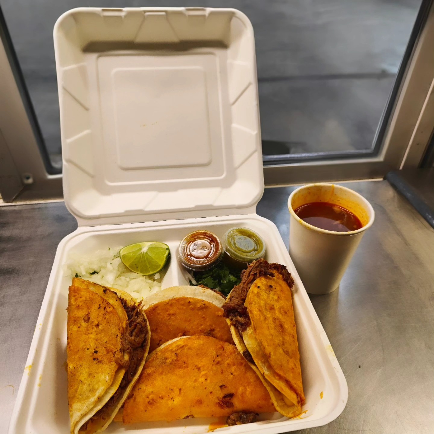 Golden tacos in takeout container with lime and red sauce