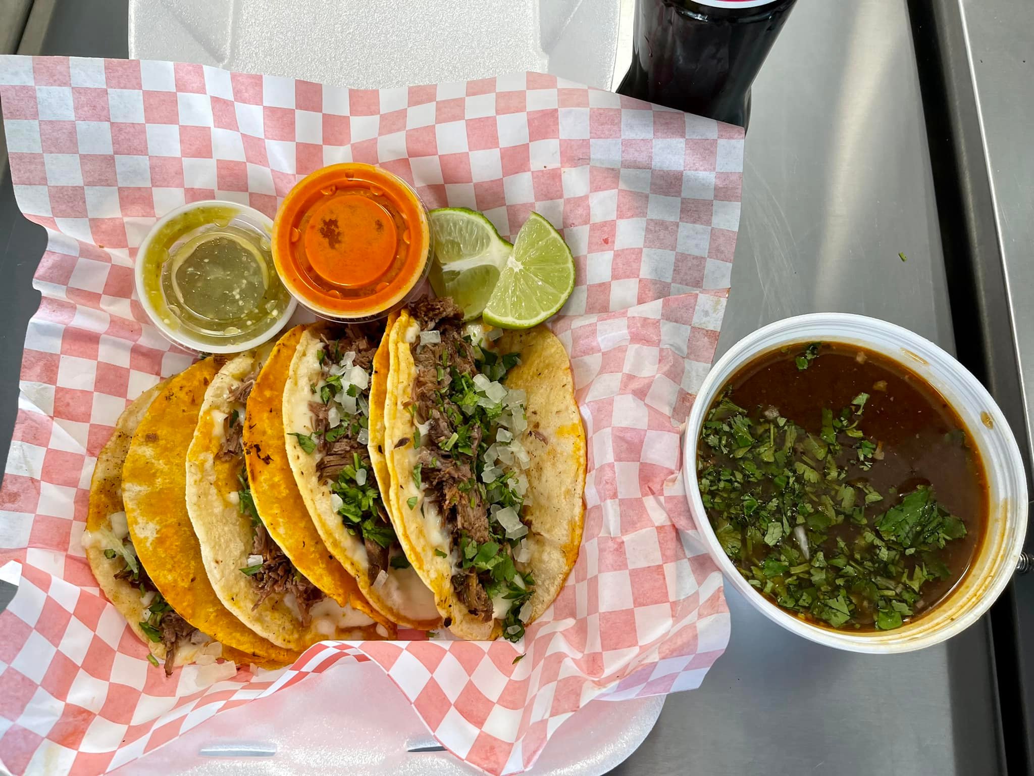 Tacos with fresh toppings, limes, and sauces on checkered paper